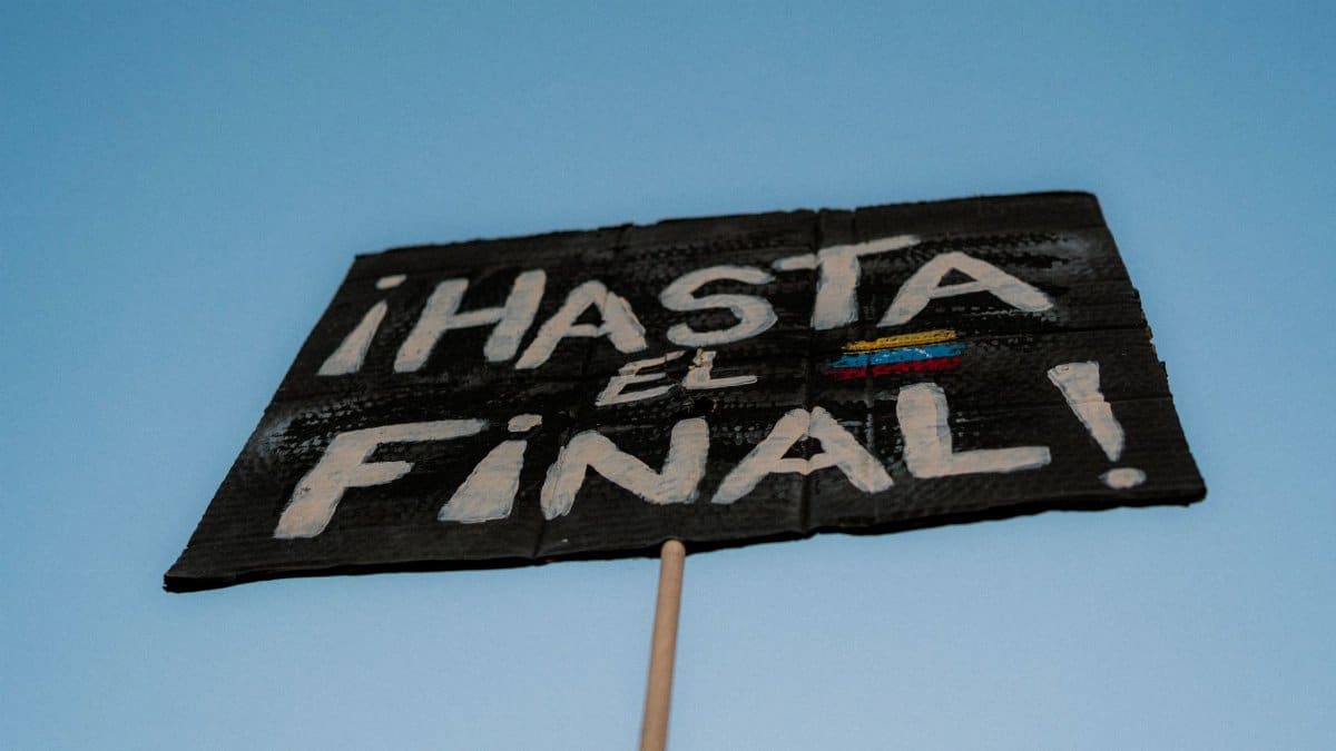 Close-up of a protest sign saying "Hasta el Final" against a clear blue sky.