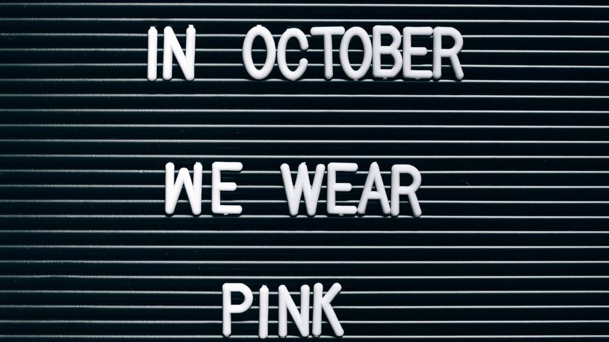 Minimalist sign highlighting breast cancer awareness in October with 'In October We Wear Pink'.