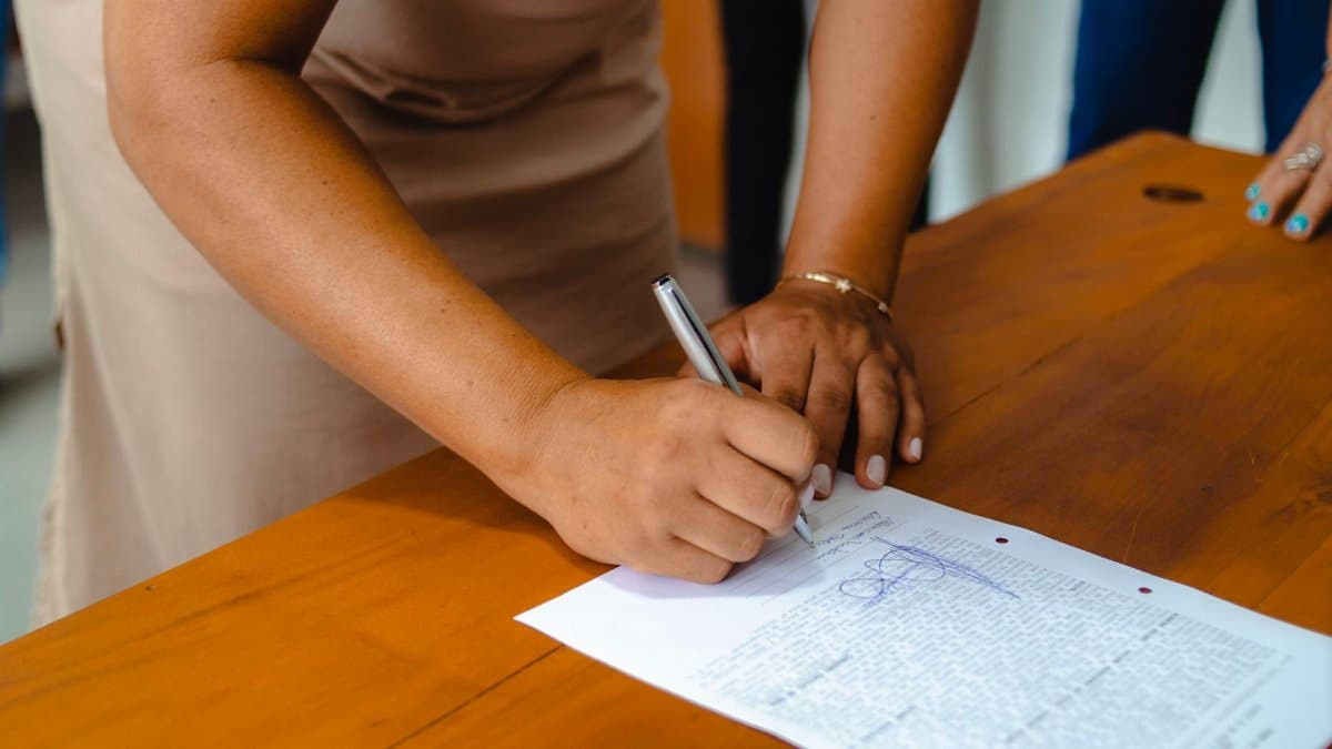 A professional woman signing an official document on a wooden table indoors.