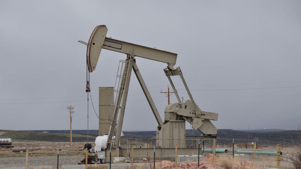 Oil pumpjack surrounded by barren landscape under overcast skies, showcasing industrial machinery.