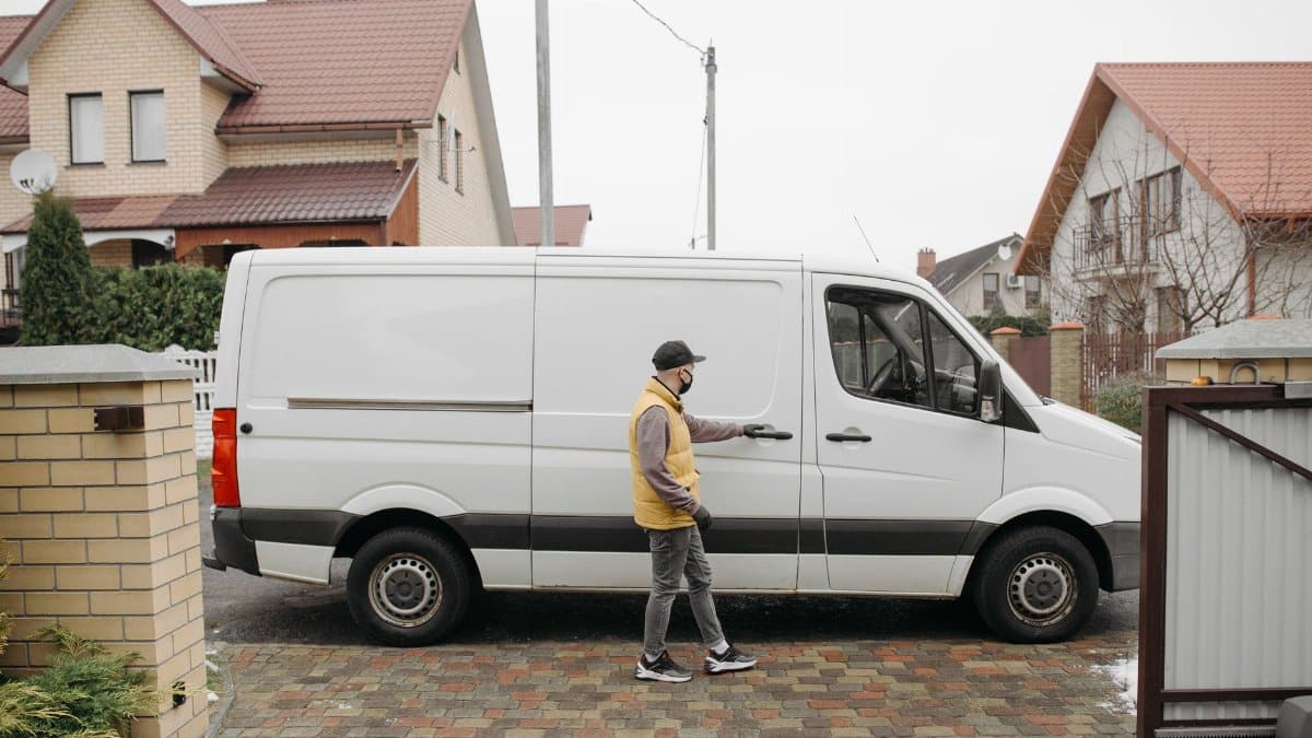 A delivery man exits his van in a suburban residential neighborhood for home delivery.