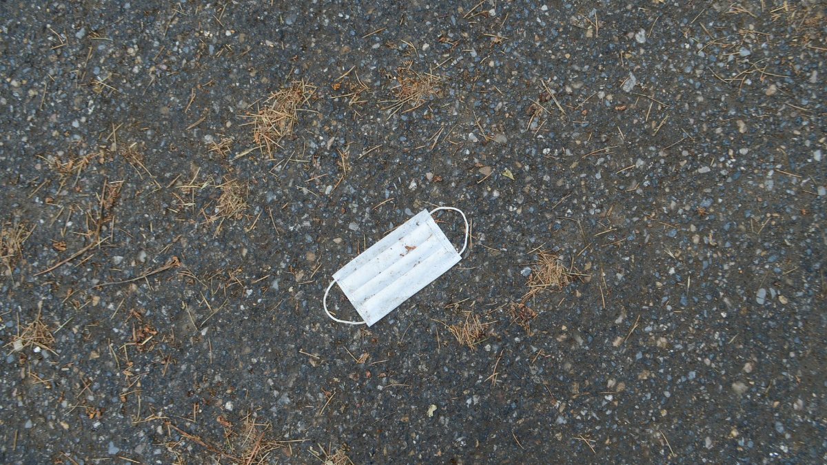 Disposable face mask lying on a rough, textured ground, emphasizing environmental litter concerns.