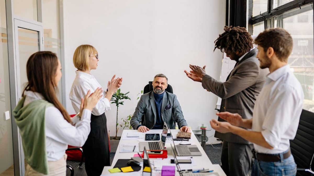 Diverse business team applauding senior leader in modern office setting.