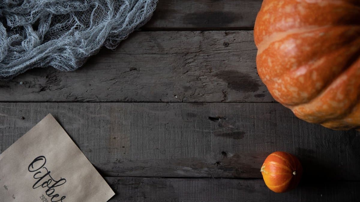 Autumn-themed flat lay with pumpkins, fabric, and an October calendar on rustic wood.