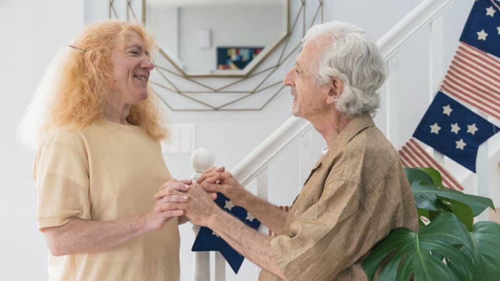 Joyful elderly couple holding hands indoors, expressing love and happiness.