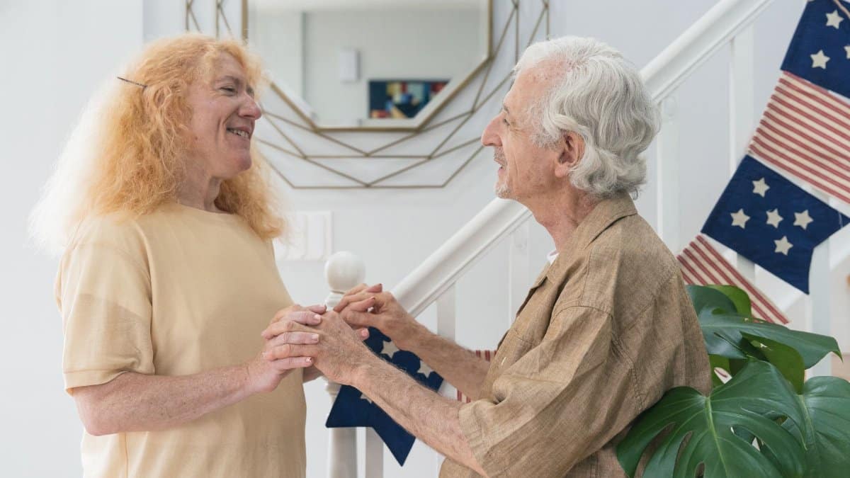 Joyful elderly couple holding hands indoors, expressing love and happiness.