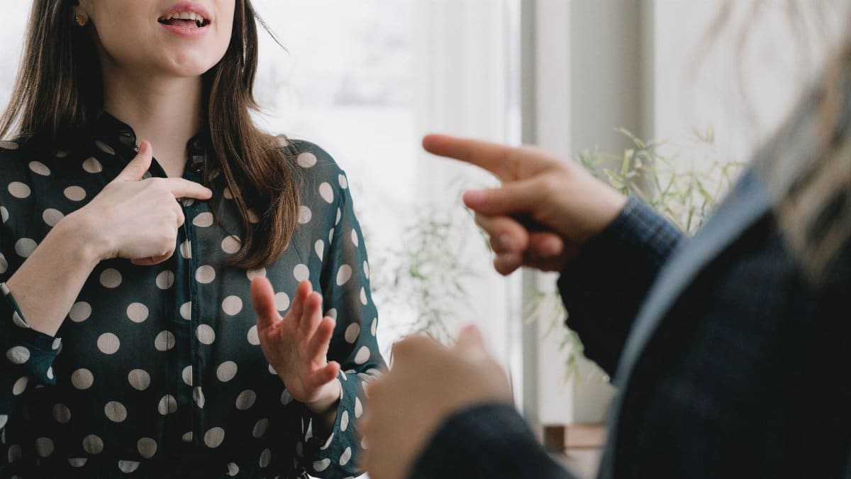 Crop unrecognizable woman in formal suit pointing at female colleague in elegant dress while standing together near window and discussing business plan in light office