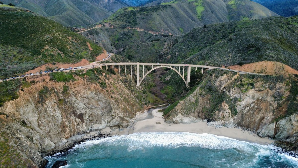 Aerial view of Bixby Creek Bridge along Big Sur coast with lush hills and the Pacific Ocean.