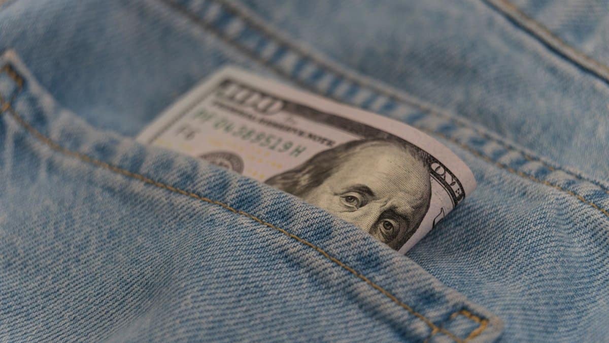 Close-up of a 100 dollar bill in a denim pocket, symbolizing finance and savings.