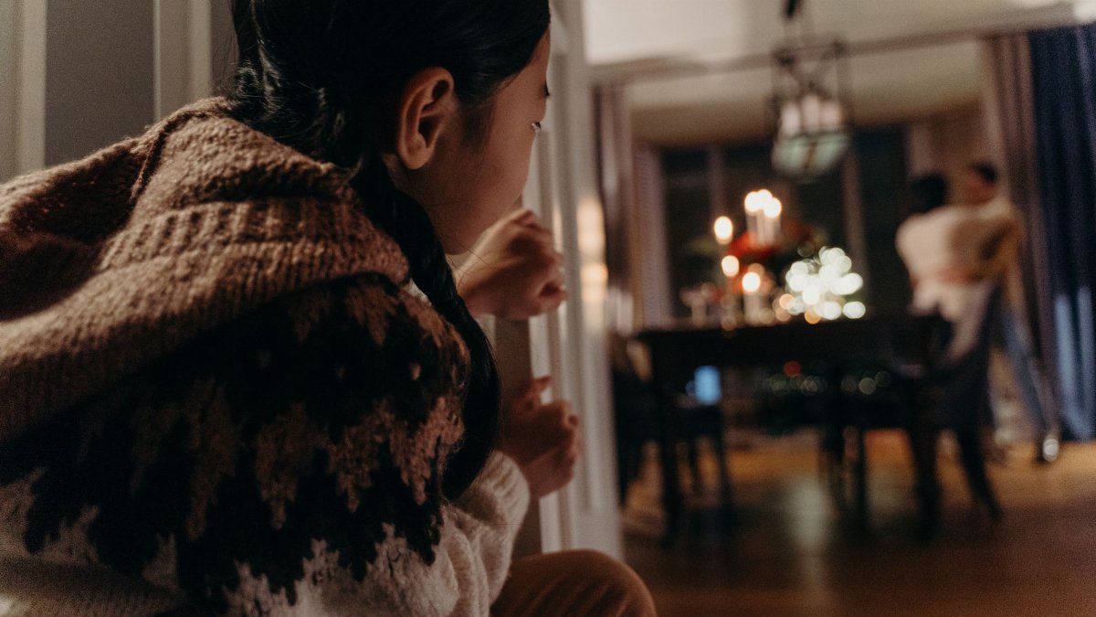 A child peeking from a doorway watching parents dance in a warmly lit room.