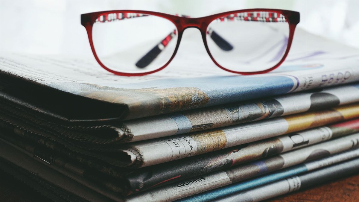 Red eyeglasses resting on a stack of newspapers symbolize reading and information.