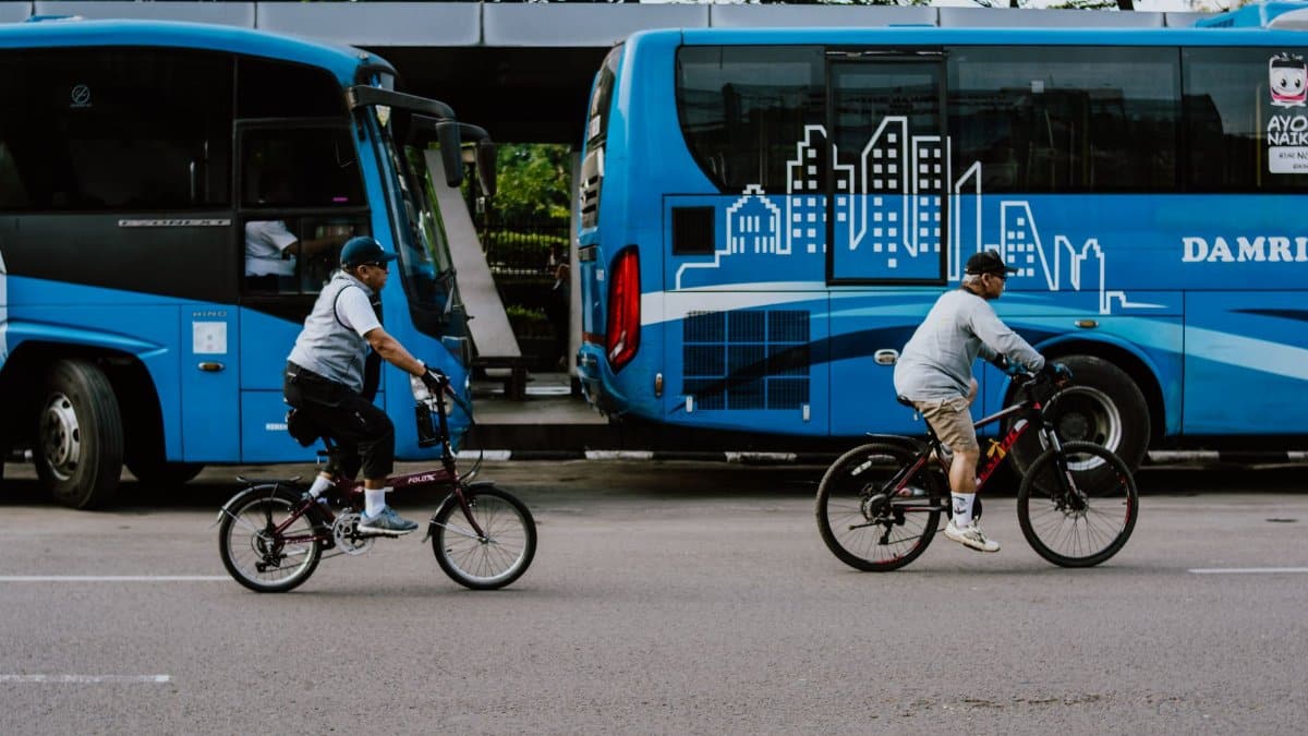Two cyclists ride past parked buses on a city street in Bandung, Indonesia.
