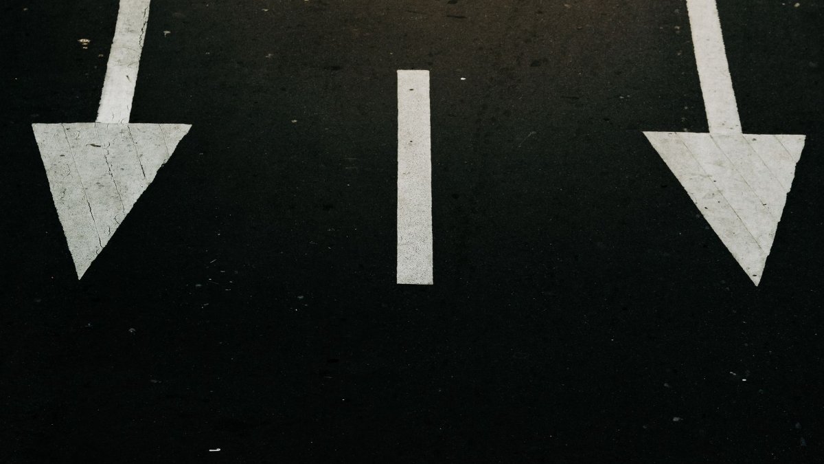 Traffic direction arrows on a city street, symbolizing decision and navigation.