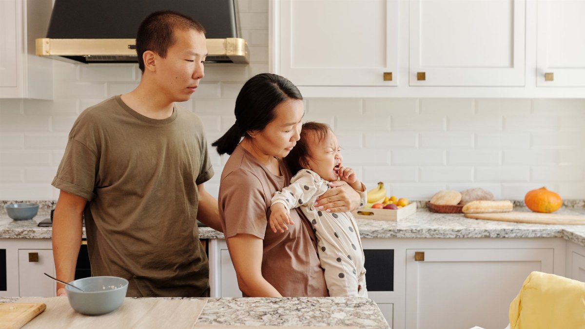 An Asian family comforts a crying baby in a modern kitchen setting, portraying parenthood and care.