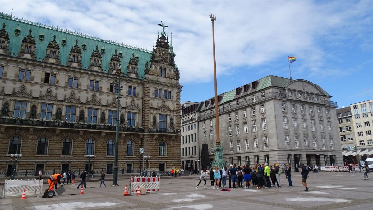 Crowd gathers at historic Hamburg Town Hall plaza under clear sky.