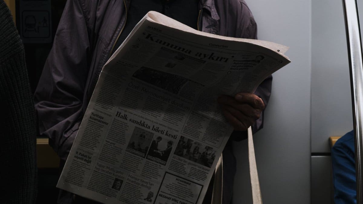 A man reads a newspaper in a dimly lit public transport setting, reflecting city life.