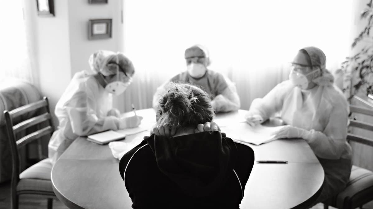 Healthcare team in protective equipment engaging with a person at a table, highlighting medical discussion in pandemic setting.