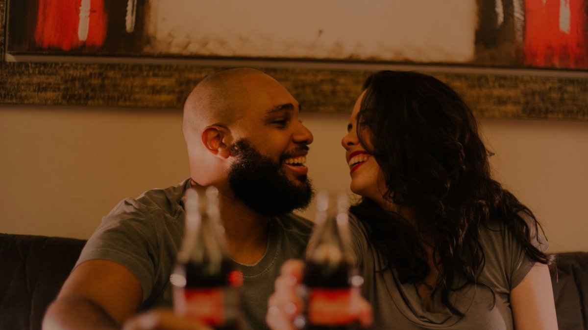 A joyful couple shares a soda and laughter indoors, capturing the essence of love and togetherness.