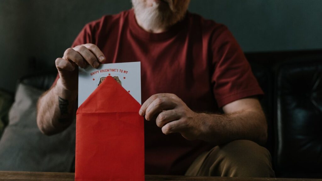 An elderly man opening a red envelope containing a Valentine's Day card, symbolizing love and connection.