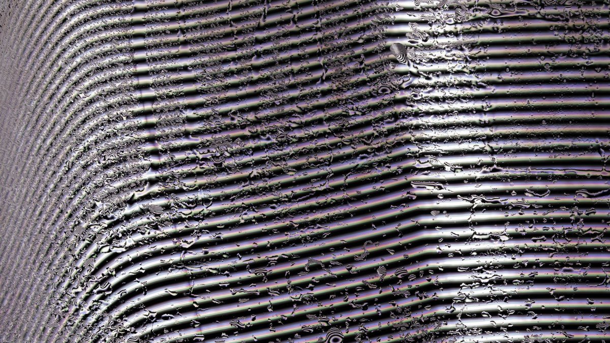 A textured pattern of water ripples on a striped metal surface with dramatic lighting.