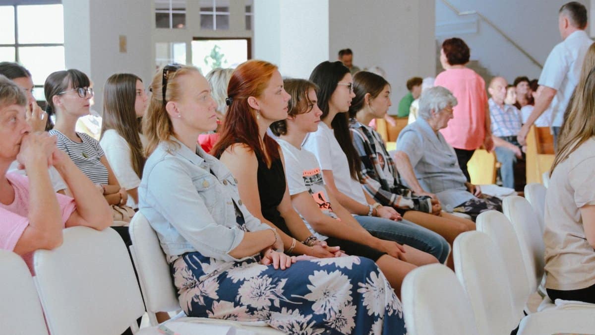 A diverse group of people sitting attentively during an indoor meeting or event, captured in a spacious room.