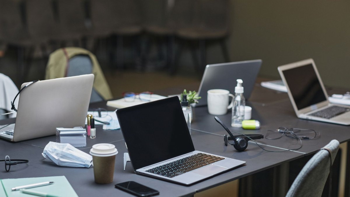 A cluttered office desk setup featuring multiple laptops, coffee cup, and office supplies for a busy workday.