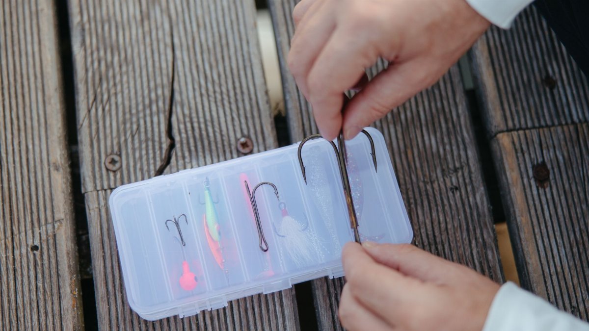 Hands organizing fishing hooks in a plastic case on a wooden surface. Perfect for fishing enthusiasts.
