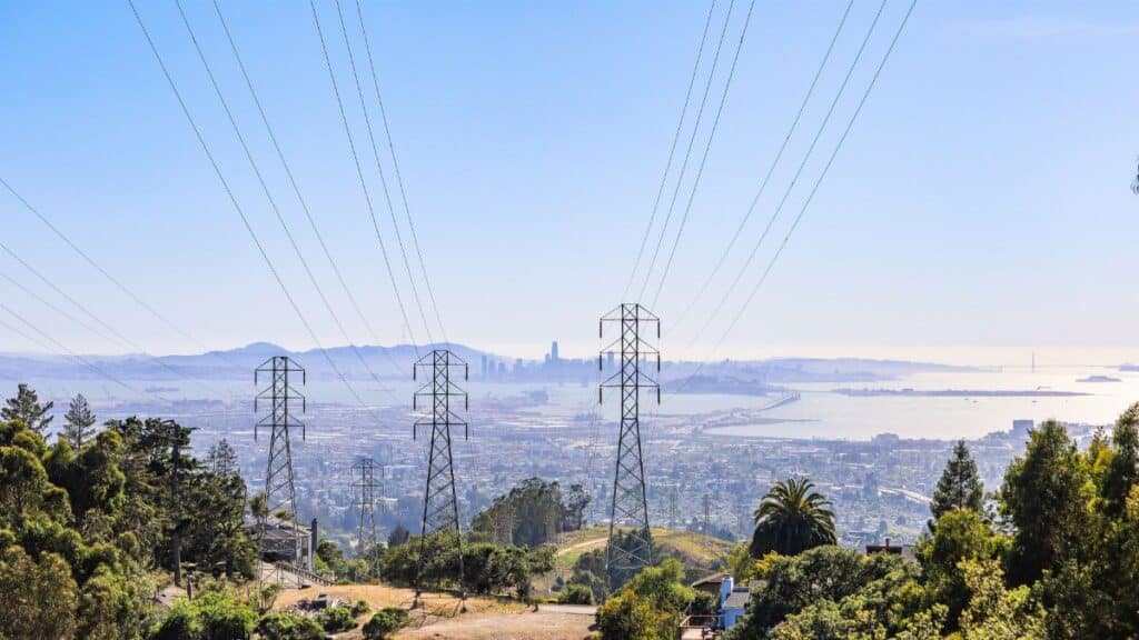 Power lines stretch over a lush landscape with city skyline in the distance.