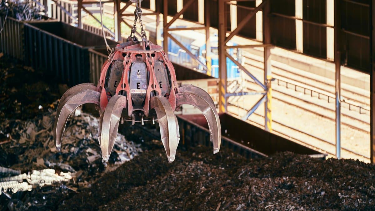 A claw crane inside a recycling facility lifting scrap metal, highlighting industrial processes.
