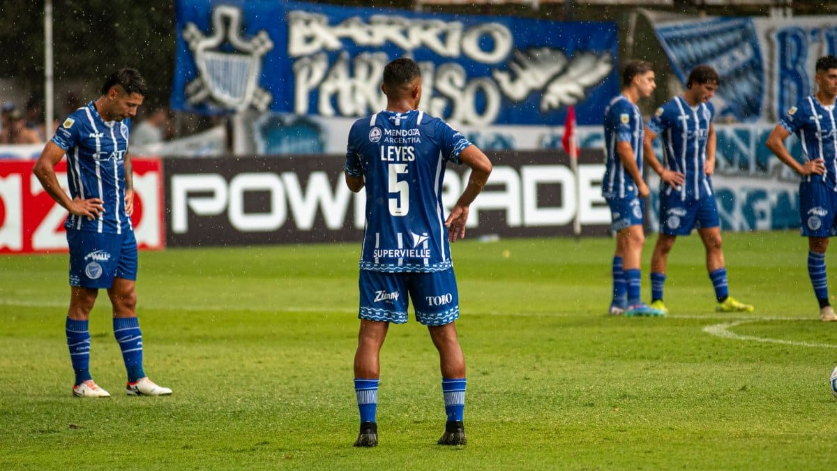 Soccer team in blue uniforms huddles on a rainy field, preparing for a match.