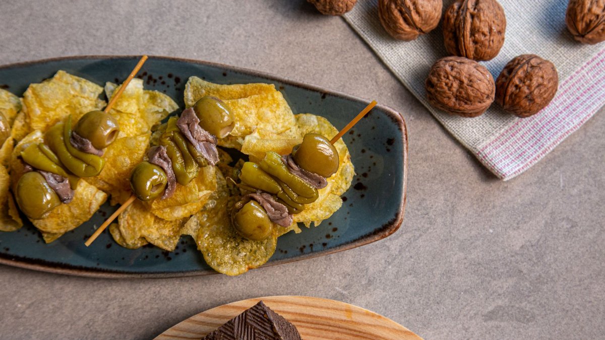 Tantalizing Spanish pincho tapa with olives, chips, and walnuts on a plate.