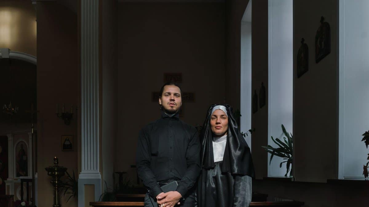 A priest and a nun standing together in a quiet church session.