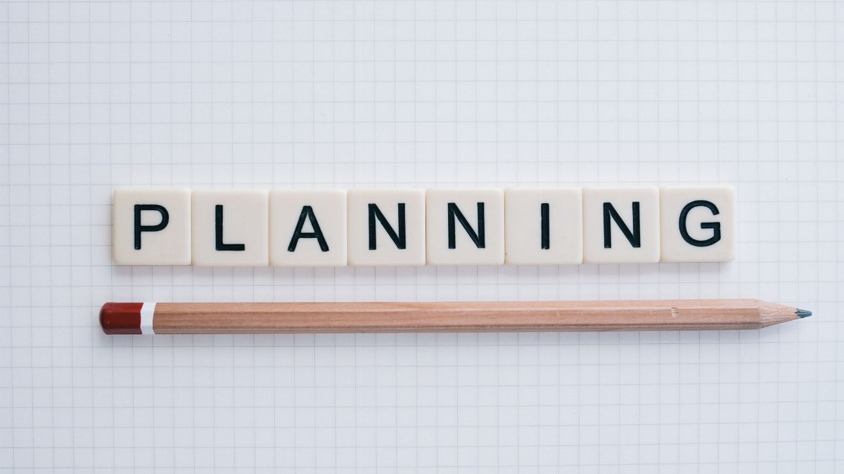 Overhead shot of letter tiles spelling 'planning' with a pencil on graph paper.