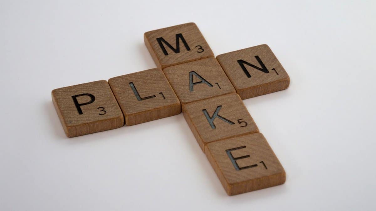 Wooden Scrabble tiles forming the words 'make' and 'plan' on a clean white background.