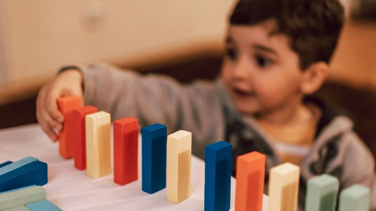 A young boy plays with colorful wooden blocks indoors, focusing intently and learning through play.