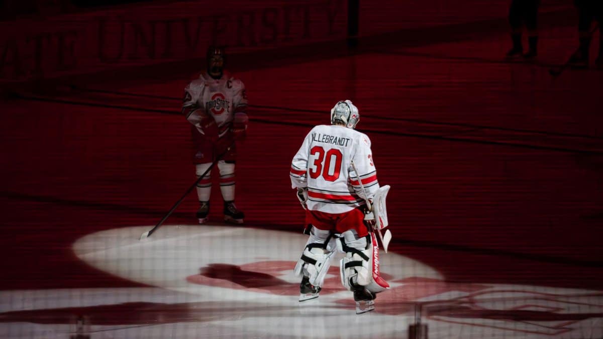 Ice hockey players in spotlight on a rink during a match under red lighting.