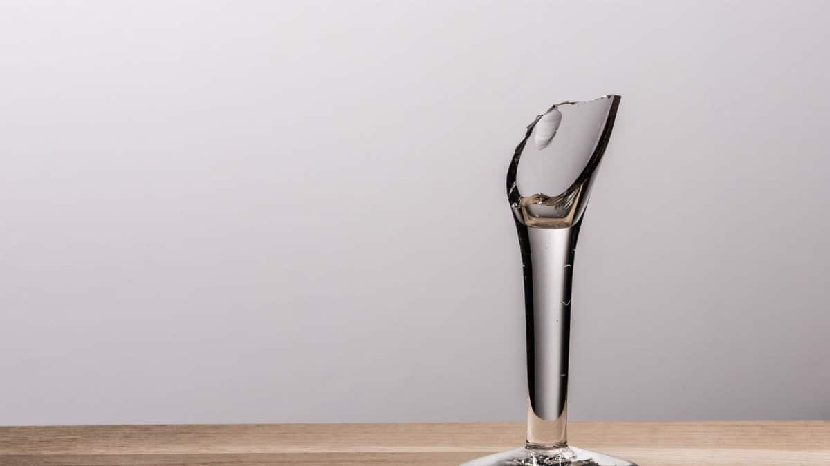 A broken wine glass on a wooden table with clear shadows and minimalist backdrop.