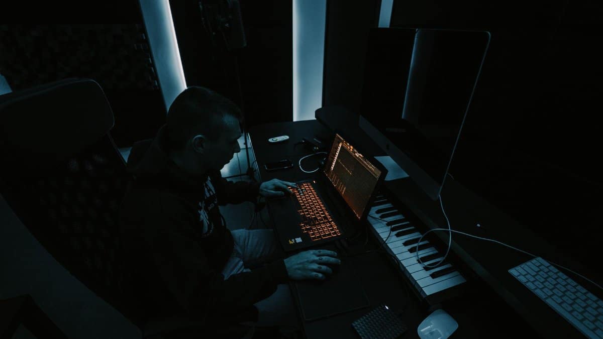Man working on audio production in a dimly lit studio with multiple screens and equipment.