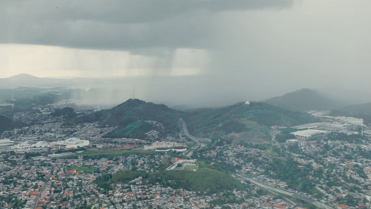 Aerial shot capturing a rainstorm approaching a sprawling urban landscape near hills.