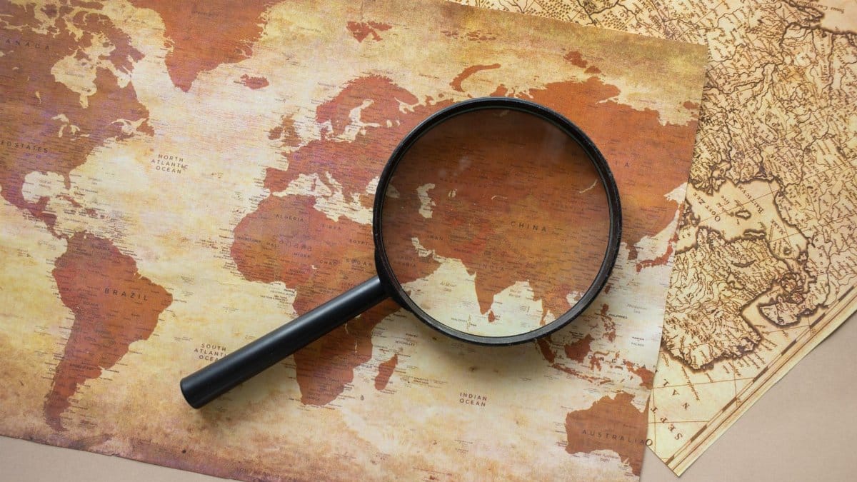 A top view of a vintage world map with a magnifying glass highlighting regions for exploration.