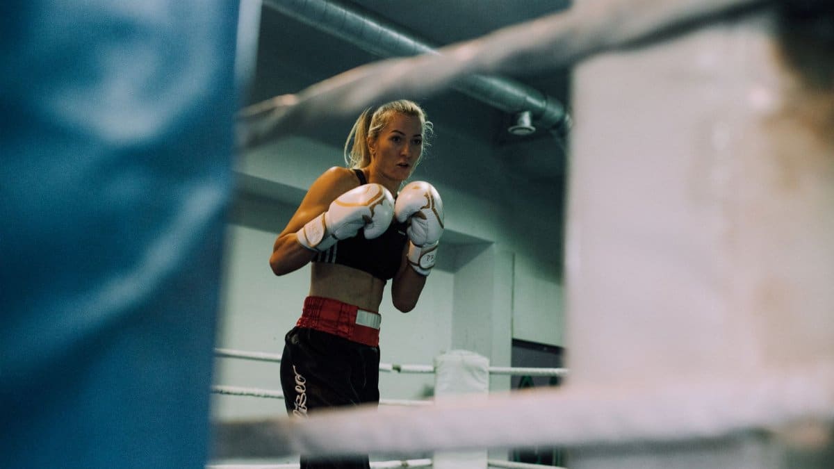 Female boxer poised in the ring, ready for a match, inside a boxing gym.