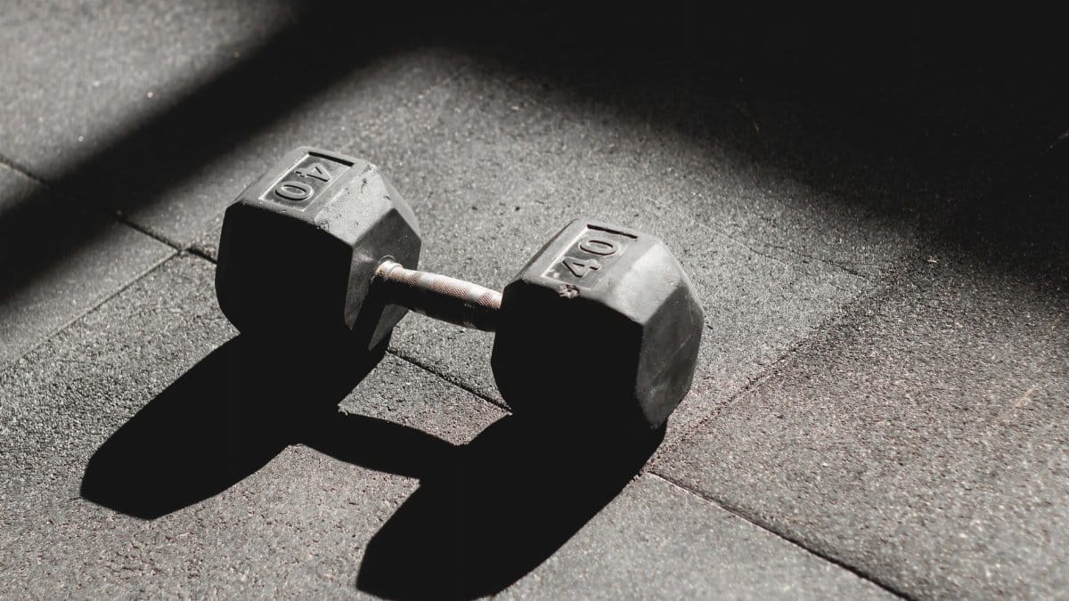 A single 40 lb dumbbell rests on the gym floor, highlighted by light and shadow play.