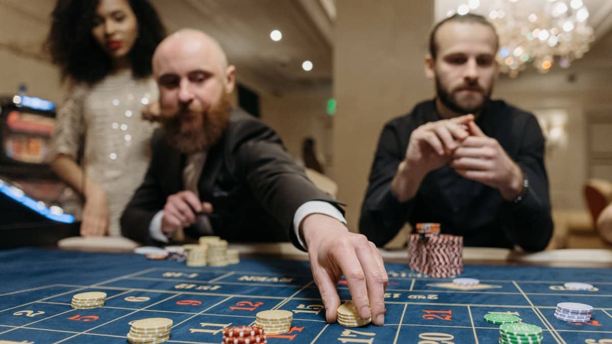 Three adults playing roulette at a casino, focused on placing bets with gaming chips.