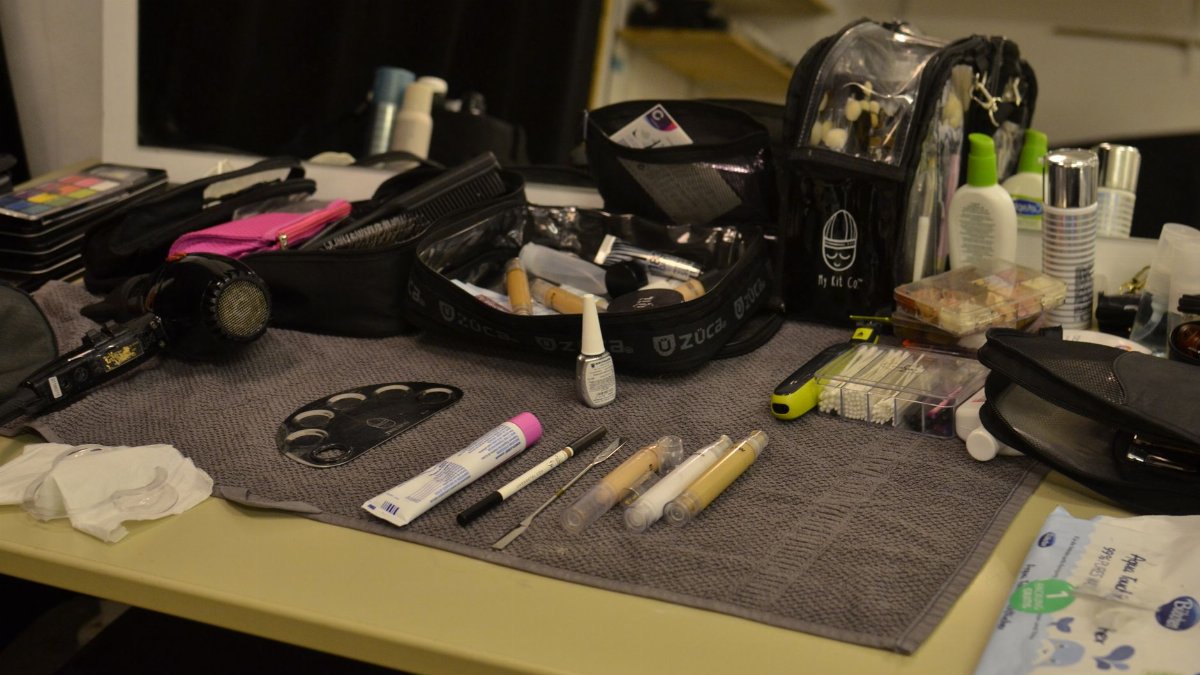 From above of hair dryer and cosmetic bags with various makeup supplies and products placed on table in dressing room