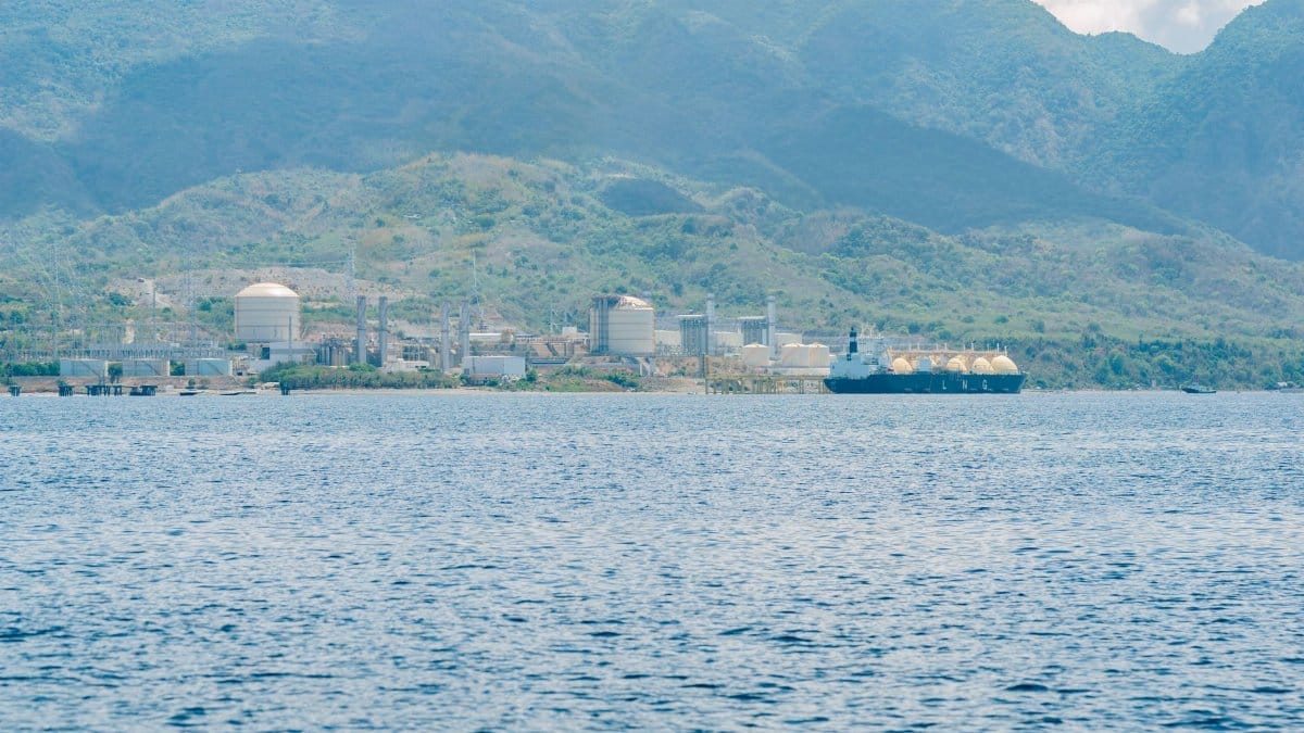 Industrial facility by the coast with a docked LNG tanker, set against mountain backdrop.