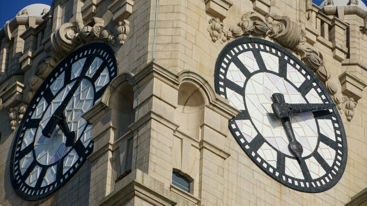 Detailed view of ornate clock faces on a historic stone tower captured in bright sunlight.