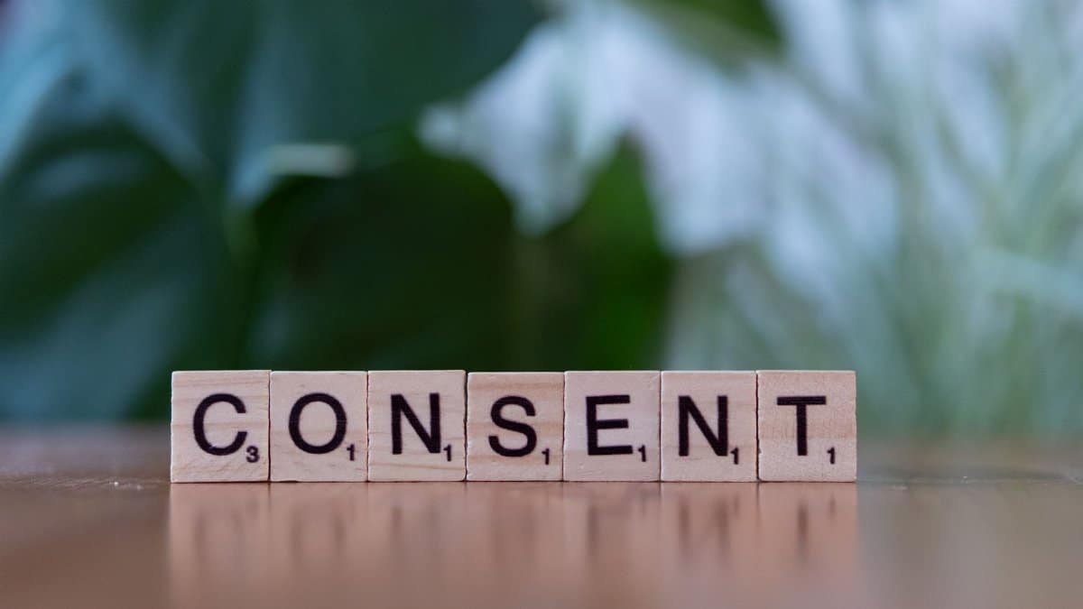 Close-up of Scrabble tiles spelling 'Consent' on a wooden table with a green blurred background.