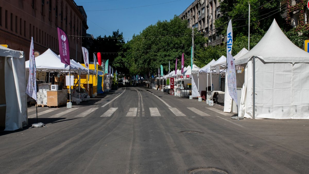 Empty street market setup with white tents and colorful flags on a clear day.