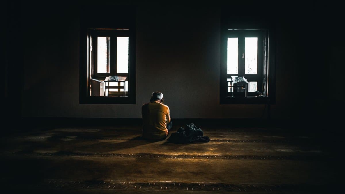 A solitary figure sits in contemplative silence in a dimly lit room with soft natural light.