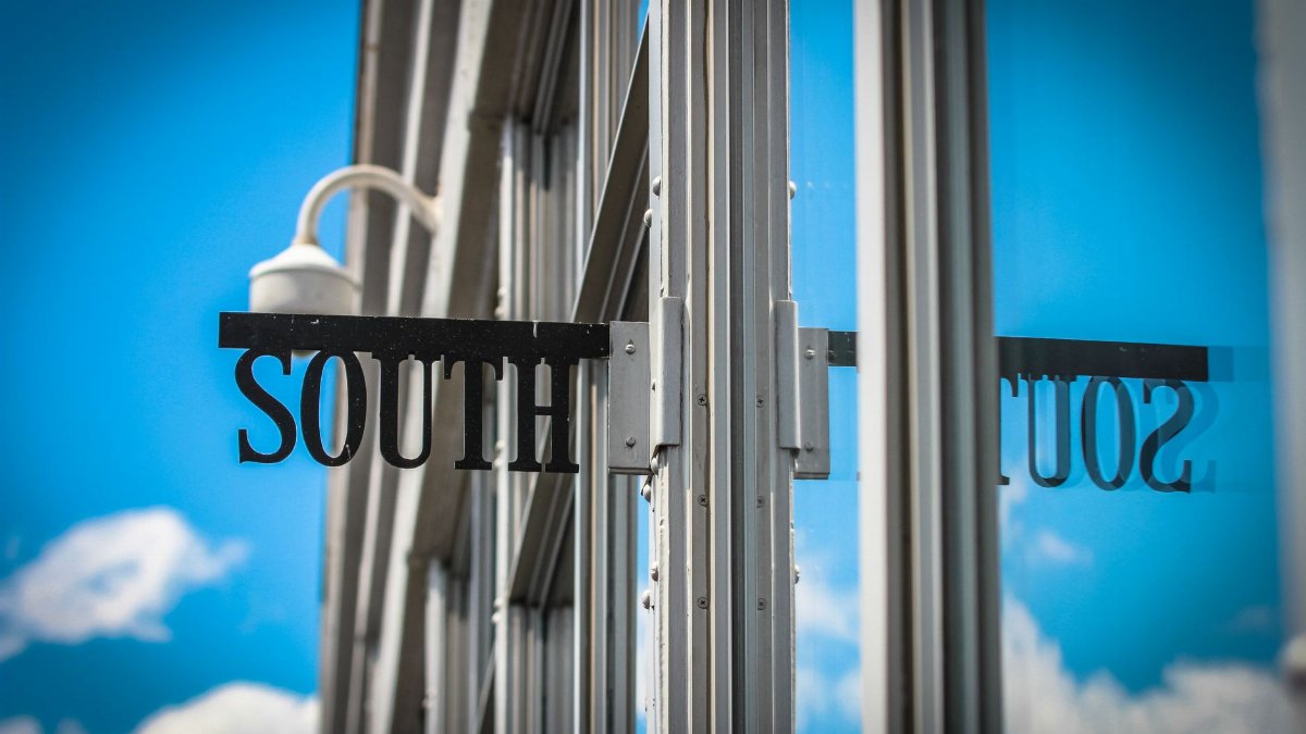 Reflection of 'South' sign on a glass building facade under clear blue skies.